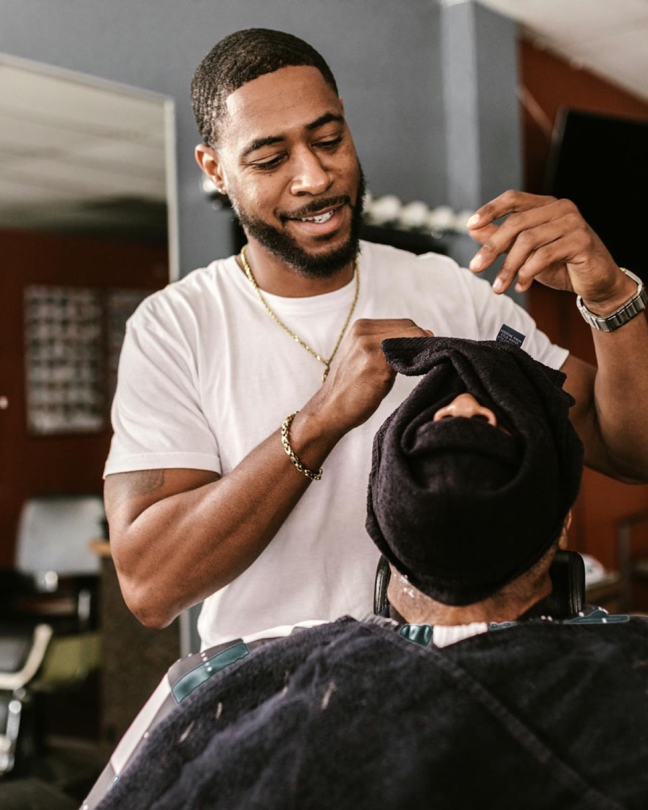 A barber holding a hot black towel over a client's face at Explicit Barbershop.