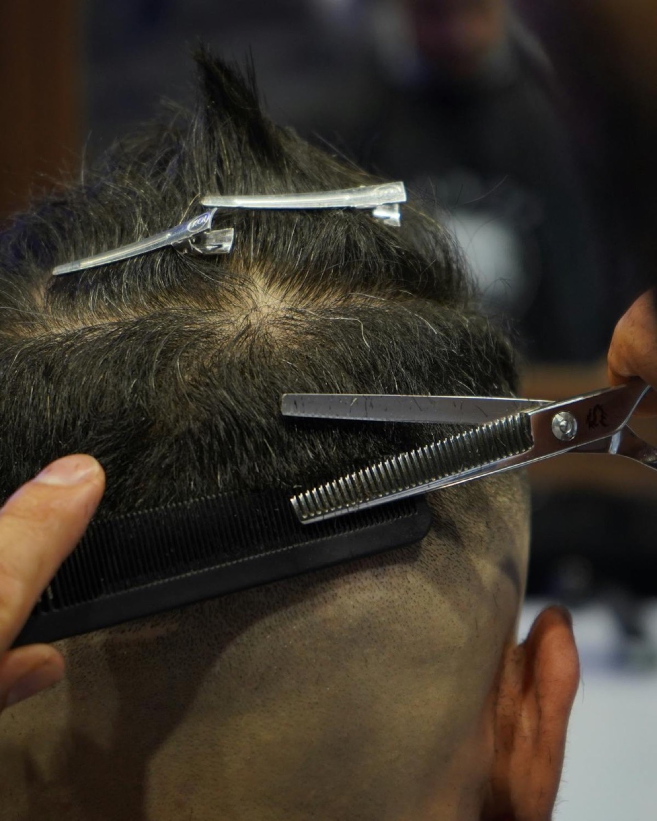 Barber using thinning shears and comb to finish a scissor cut at Explicit Barbershop.