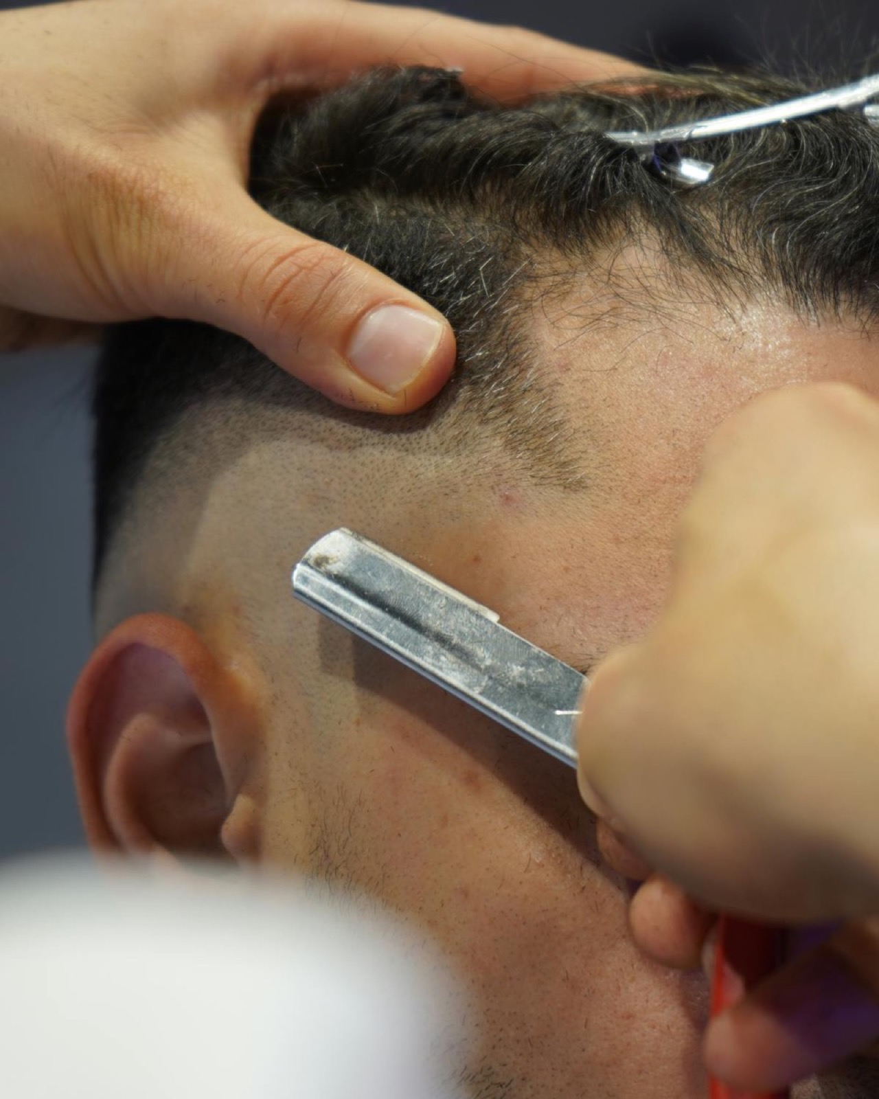Close-up of a sharp skin fade being shaped with a straight razor at the temple.