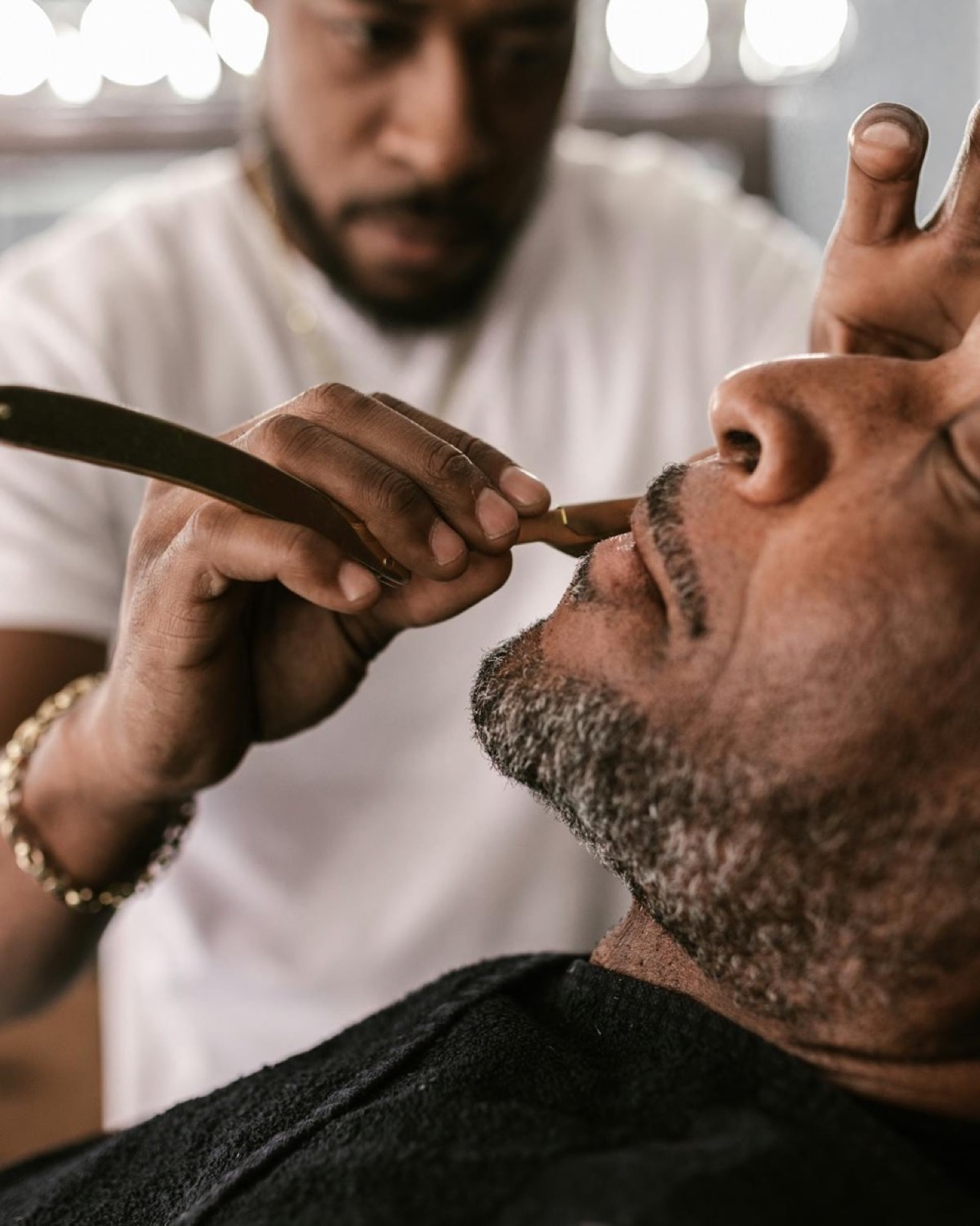 Barber giving a straight-razor mustache trim under warm vanity lights at Explicit Barbershop.