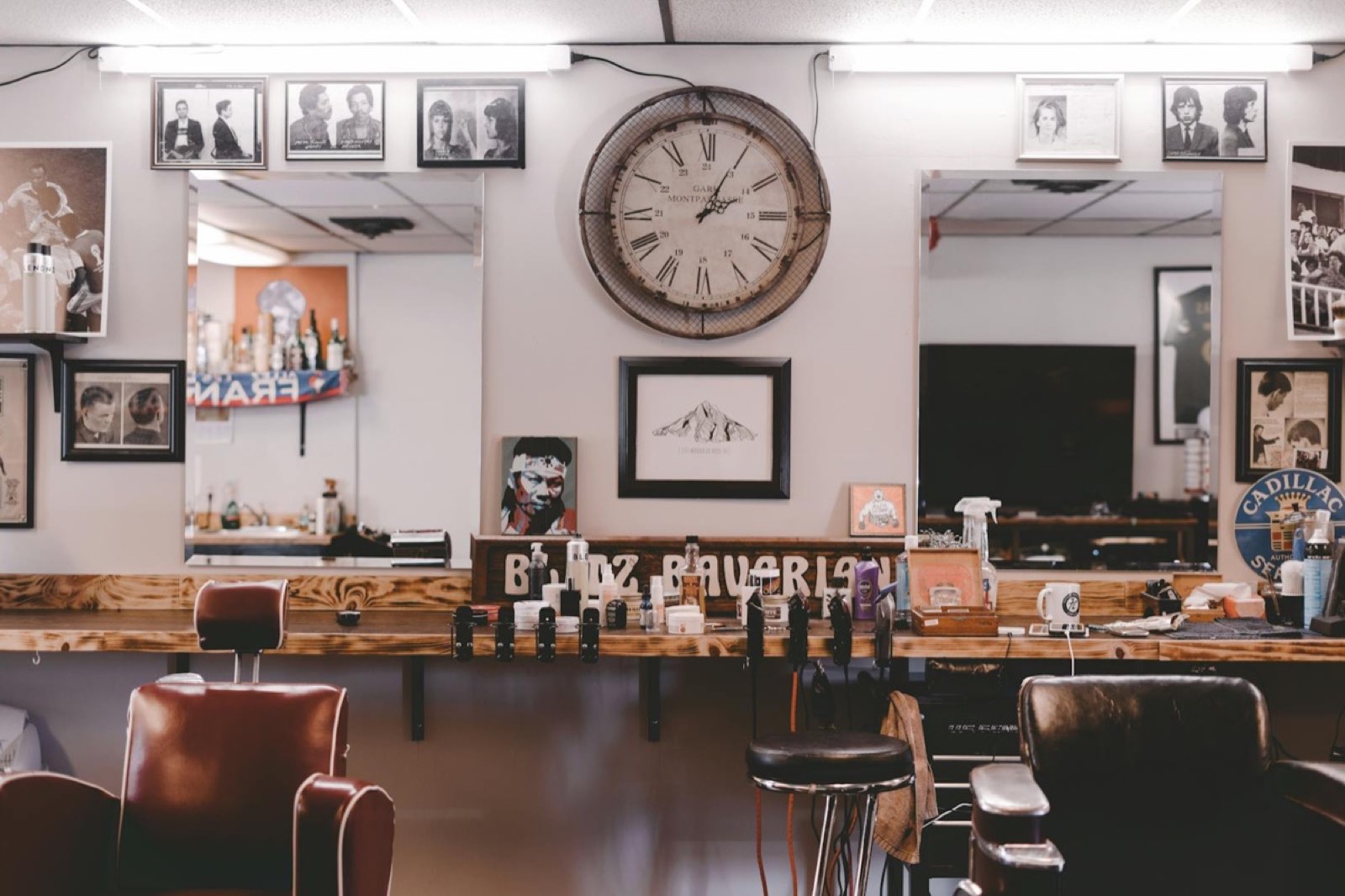 Wall of framed portraits and a vintage clock at Explicit Barbershop on 30th, North Park, with warm tungsten light spilling over the bench.